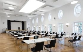 Großer Seminarraum mit Tischen und Podium für Veranstaltungen.